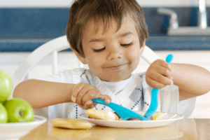 Happy Child enjoying his meal and using a knife and fork